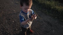 Young happy boy playing outside throwing dirt in slow motion in sunlight during sunset.