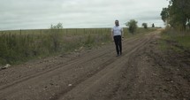 Young man walking on unpaved, dirt road on summer day explore, hiking, worshipping and praying. Lifestyle, worship and prayer concept.