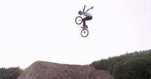 BMX rider does no hander trick over large outdoor dirt jump - wide shot