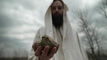 Jesus Christ holding a rock or stone in the wilderness temptation by Satan in the gospel stories.