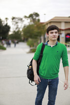 A young man walking down a sidewalk with a backpack.