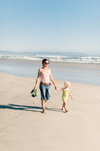 mother and daughter walking holding hands on beach 