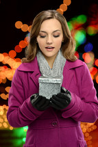 a woman in a winter coat holding a wrapped gift 