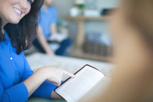 Smiling woman pointing to page of open Bible.
