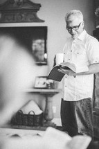 man standing holding a coffee cup and reading a Bible