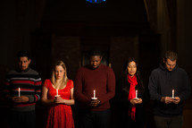parishioners with bowed heads holding candles at a Candlelight Service 