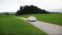 car driving on a rural road surrounded by green grass 