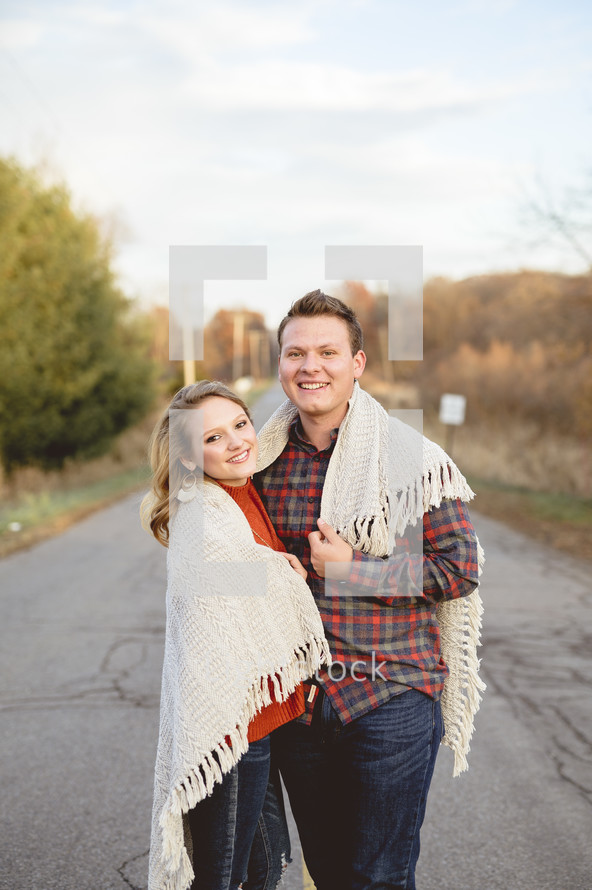 a couple standing outdoors on a path wrapped in a blanket 