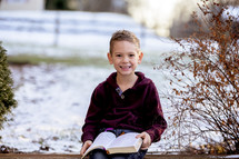 smiling boy reading a Bible outdoors in snow 