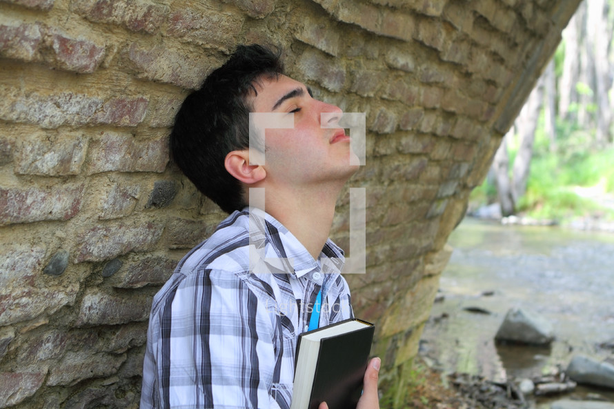 man with head tilted up holding a Bible close to his heart