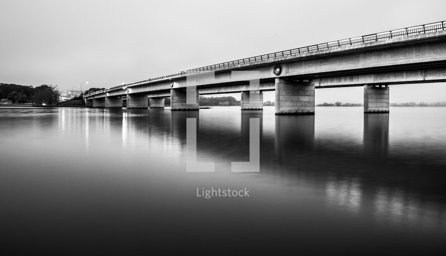 A long concrete bridge over a calm lake.