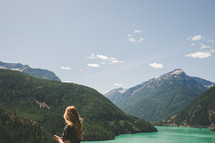 A woman stands overlooking a lake among mountains.