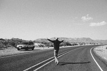 man with open arms standing in the middle of a road 