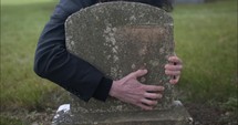 Sad, grieving man embracing family tombstone in cemetery crying in cinematic slow motion. 