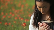 a woman holding a Bible against her chest praying in a meadow of flowers 