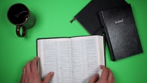 a man reading a Bible at a green desk 