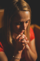 a woman sitting with praying hands in a church pew 