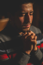 A latino man with praying hands sitting in church 