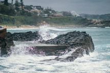 Ocean waves crashing upon rocks near a beach community.