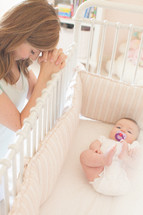 mother praying next to a baby in a baby crib