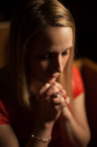 a woman sitting in a church pew with praying hands 