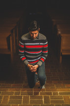 latino man kneeling in prayer in the aisle of a church 