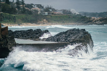 Waves crashing upon a rocky shore near a beach community.