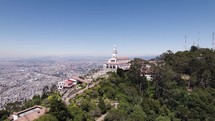 Aerial orbiting shot of Monserrate Sanctuary on Hilltop, Bogota Cityscape in Background, Colombia