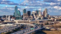 Aerial hyperlapse of downtown Dallas skyline and traffic in late afternoon with clouds in the background.	