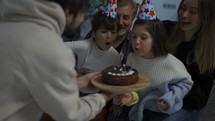 Little brother and sister blows out the candles on cake together in a circle of happy family.