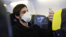 Man in respiratory mask travelling on an airplane during pandemic times takes a selfie.