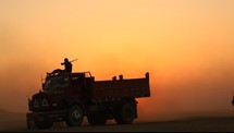 trucks driving in desert at sunset with men carrying rifles 