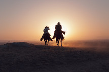 cowboys riding horses at sunset 