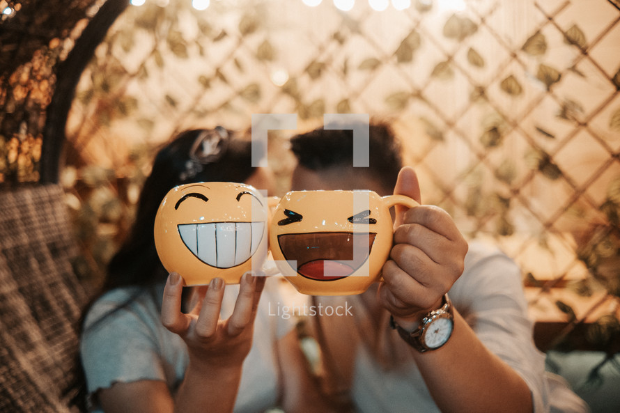 couple holding up smiley face mugs 