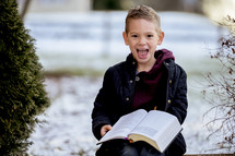 boy child holding a Bible standing outdoors in snow 