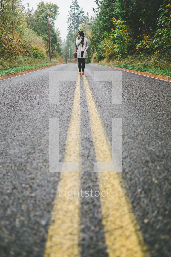 A woman standing on double yellow lines in the middle of a highway.