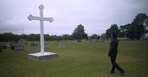 Young man in black suit looking at cross praying in worship in cinematic slow motion.