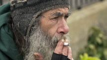 Gray bearded man smoking a cigarette on the street.