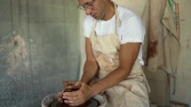 A happy young potter forms a piece of clay on a special potter's wheel in his studio. The concept of a traditional profession.