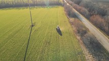 Drone footage tractor spreading artificial fertilizers in green field. Farming tractor spraying on field with herbicides. Industrial machine fertilizing a field.Chemicals used by agricultural tractor.