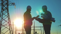 Handshake of two men people work industry. Engineers shaking hands at the construction of high-voltage power. Team engineers looking plan. Silhouette two engineer standing on field at sunset time.