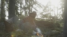 a man sitting near a campfire in a forest 