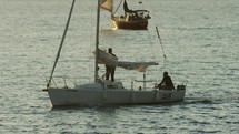 Man puts ties up sail on sailboat while approaching harbor during sunset, slow-motion