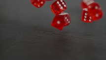 multiple red dice falling on black slate table.