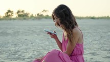 Girl in pink dress Using phone on the beach near ocean