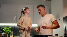 A happy little brown-haired girl in a cream sweater together with her middle-aged dad preparing dinner.