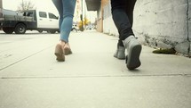 legs of a couple walking on a sidewalk 