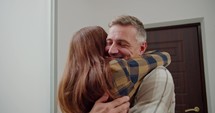 A happy middle-aged man with gray hair in a plaid shirt returns home and is greeted by his brunette wife in a plaid shirt in a modern apartment during the day