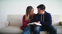 a couple sitting on a couch reading a Bible 