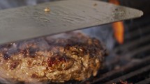 Slow motion of beef hamburger on a grill in close up with flames and smoke